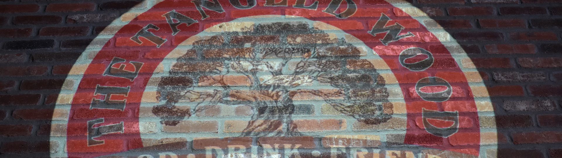 The Tangled Wood logo printed on a brick wall.