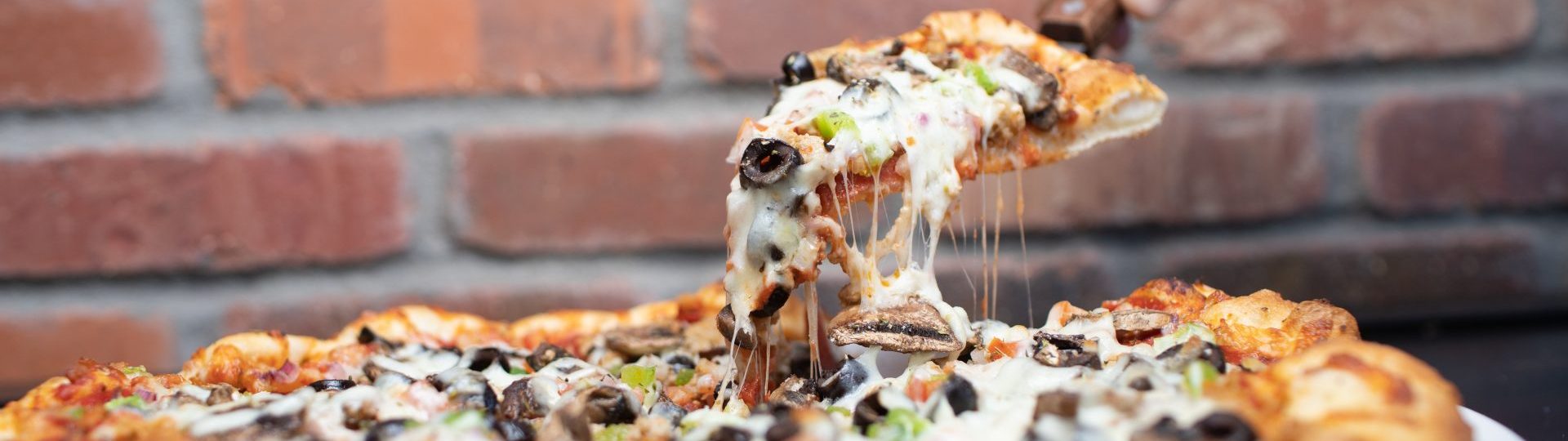 Pizza with lots of toppings and thick crust, and a hand pulling a piece out with a serving utensil.